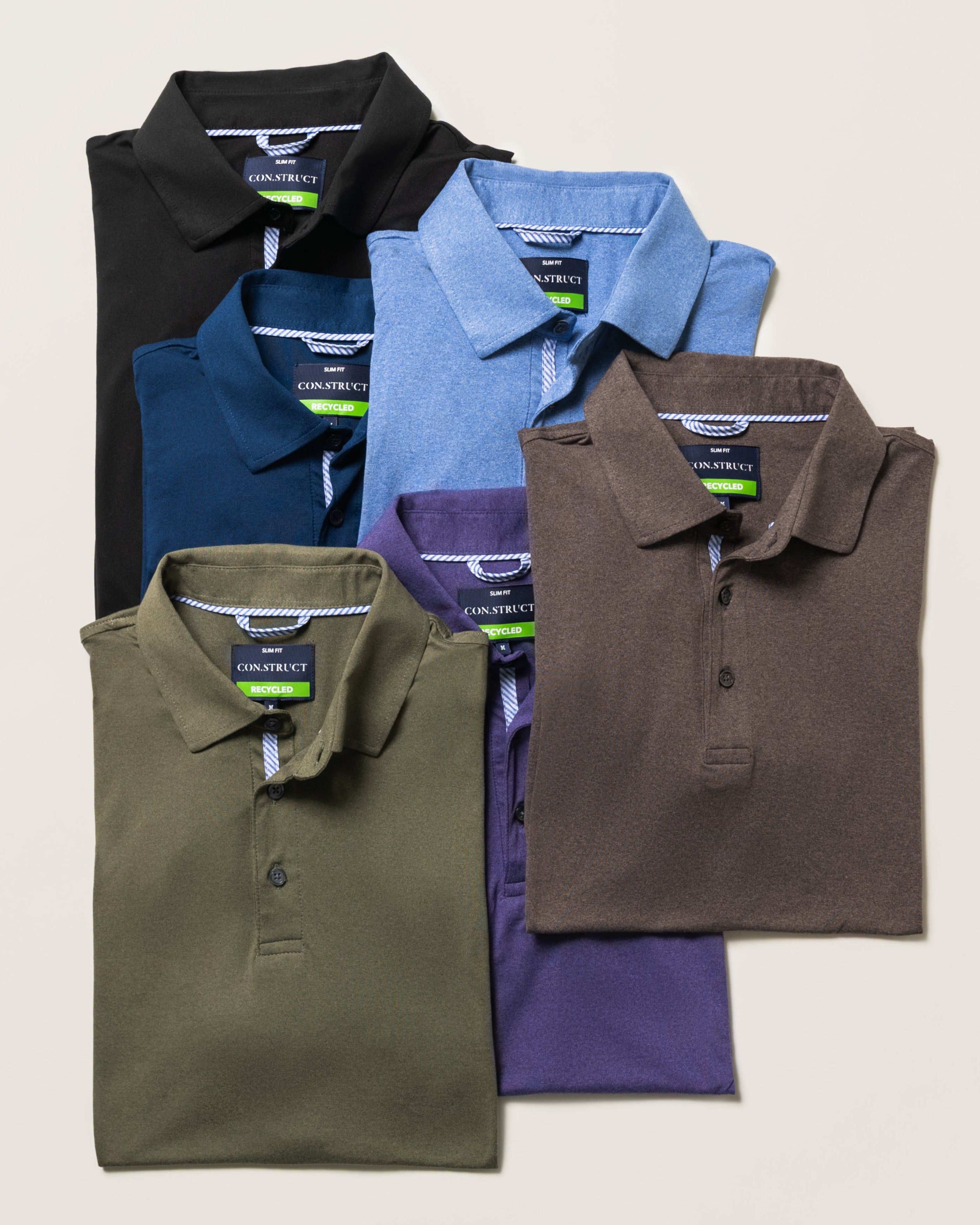 Five folded short-sleeve polo shirts in black, navy, light blue, olive green, brown, and purple, arranged in a fan-like stack on a light beige background.