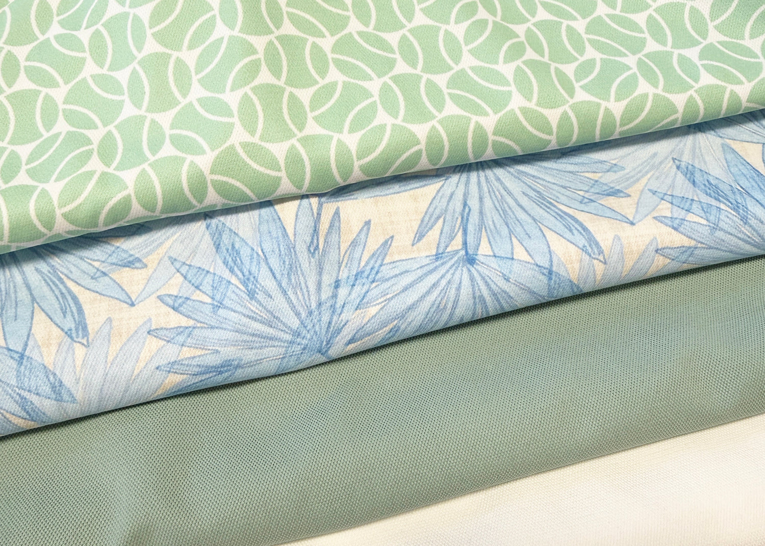 Stack of fabric swatches with green leaf pattern, blue floral pattern, solid green color, and white color.